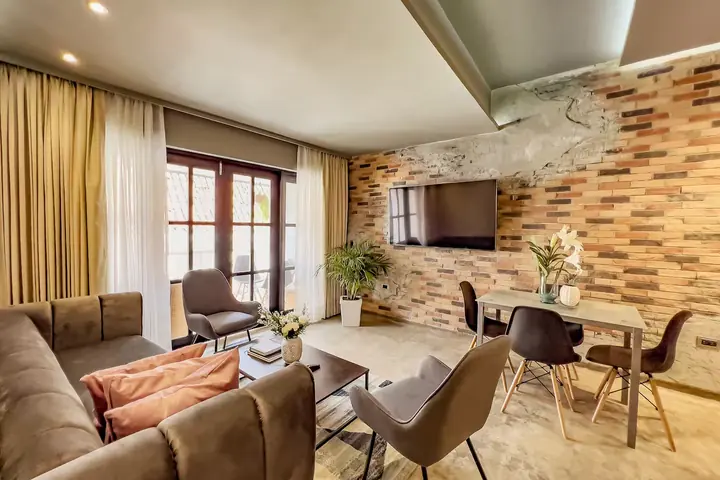 Living and dining room with a brick feature wall, sofa, wall-mounted TV and doors to the balcony