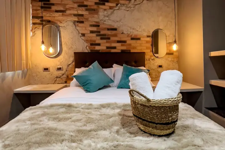 Bedroom with a large bed, teal cushions and a brick wall with pendant lights