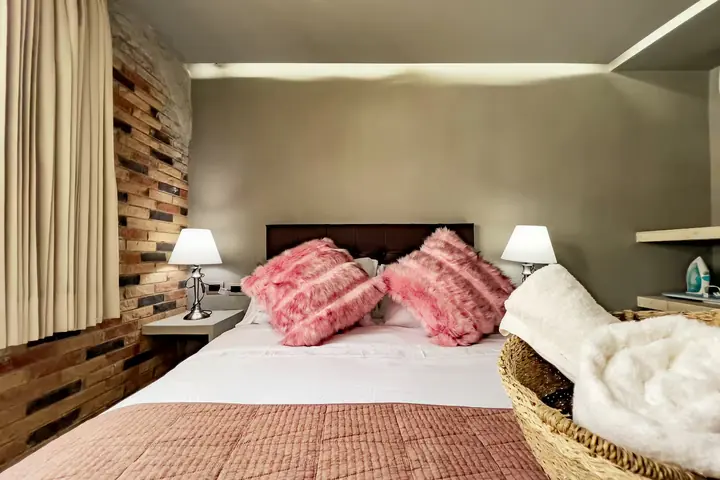 Bedroom with a queen bed, pink cushions and bedside lamps