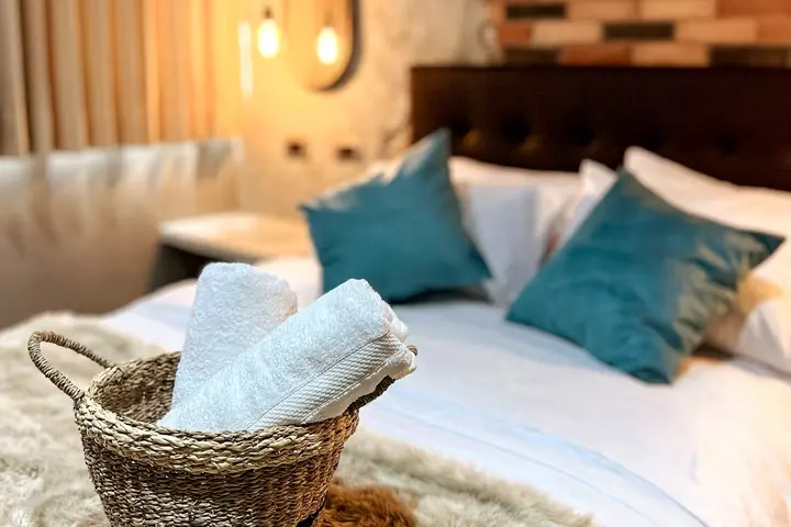Bed with teal cushions and a basket of rolled towels