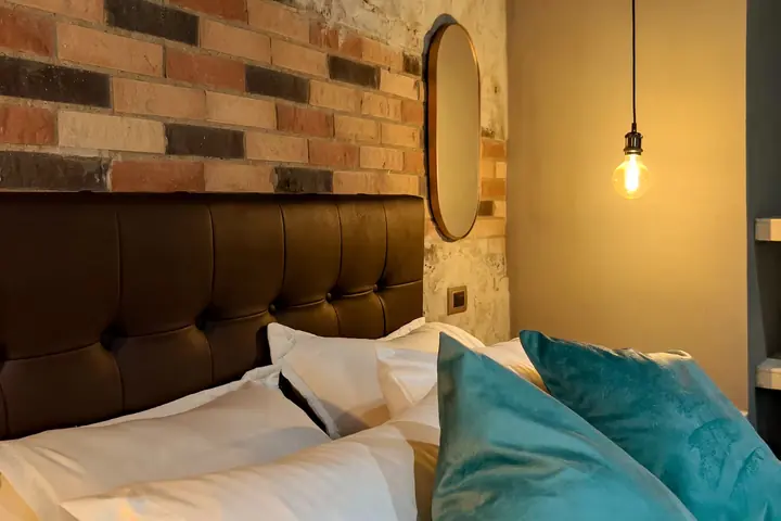 Upholstered headboard against a brick wall with an oval mirror