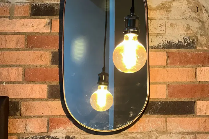 Pendant bulbs in front of an oval mirror on a brick wall