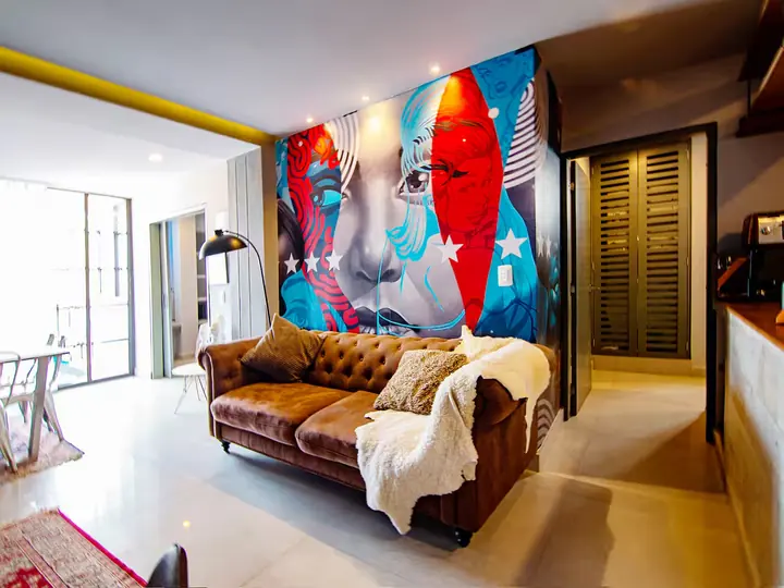 Living room with a large colourful mural, leather Chesterfield sofa and doors to the balcony
