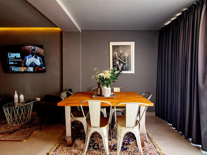 Dining table with white metal chairs, TV and dark curtains