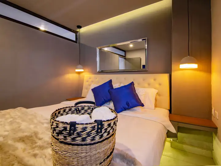 Bed with blue cushions, towel basket and warm indirect lighting